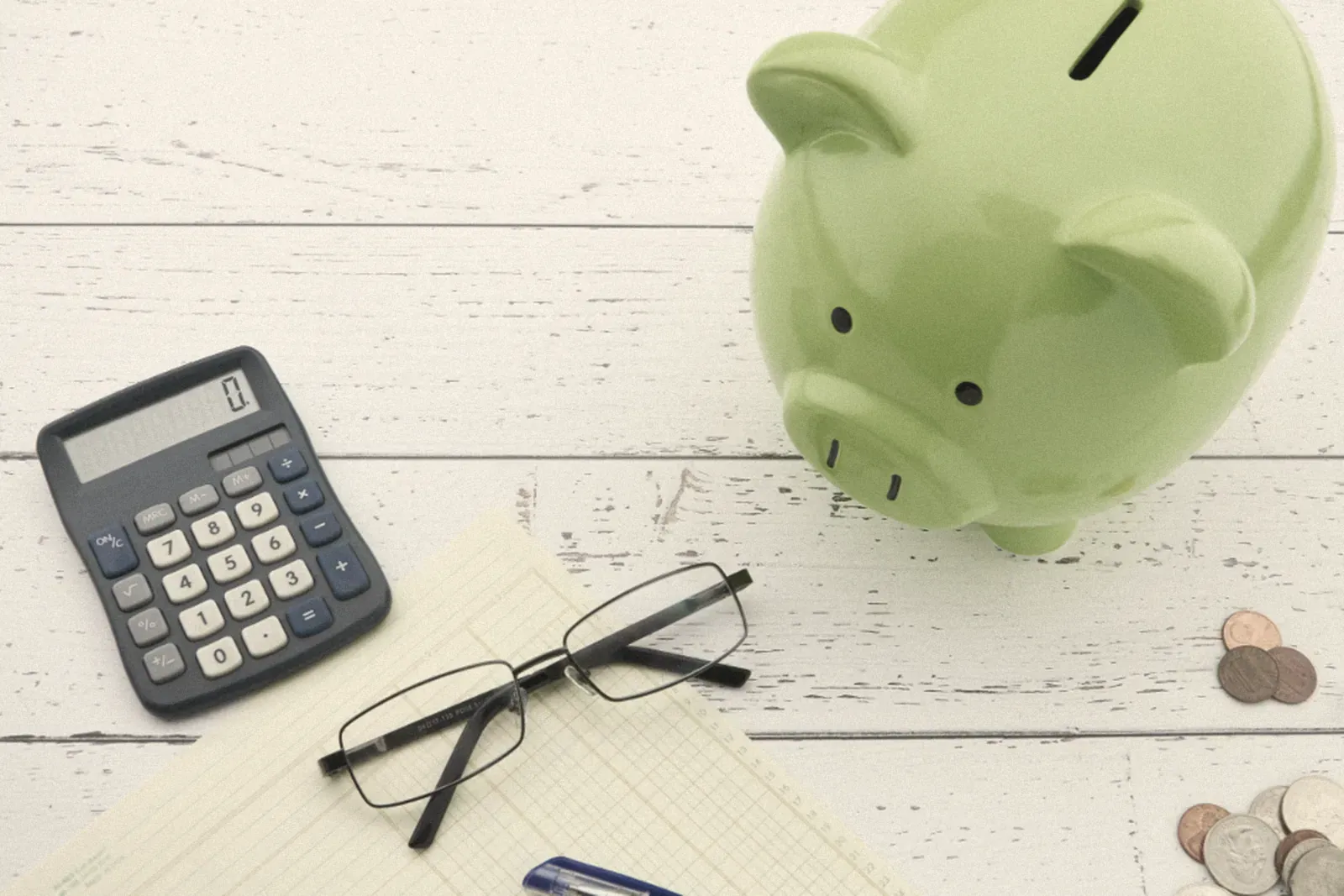 A piggy bank next to a calculator and glasses
