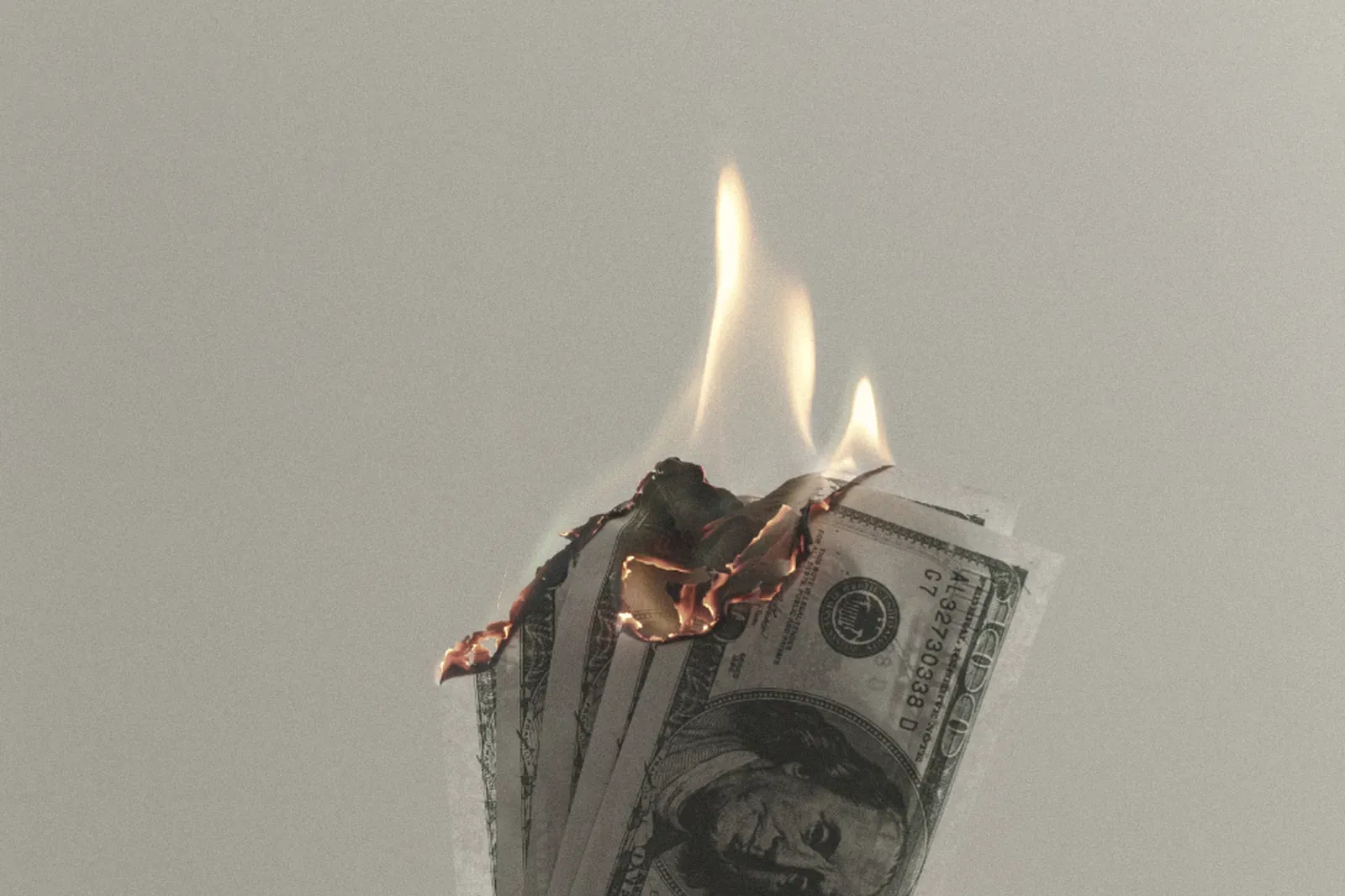 A hand holding burning dollar bills