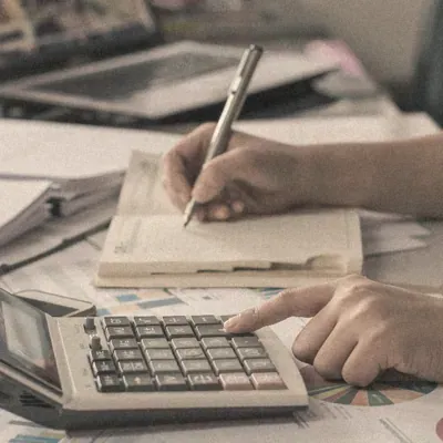 A person writing in a ledger beside a calculator